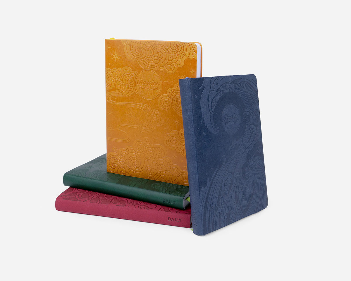 Four colorful planners with eastern elements stacked on a white background