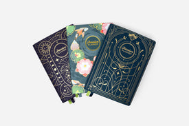 Three decorative planners with floral and celestial designs on a white background