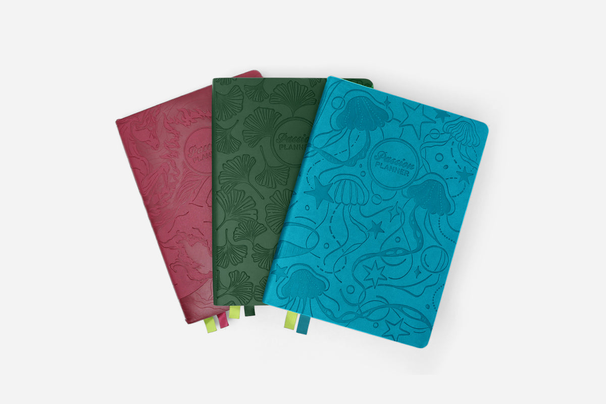 Three planners with embossed designs in red, green, and blue on a white background