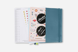 Teal planner with stickers and open pages on a white background