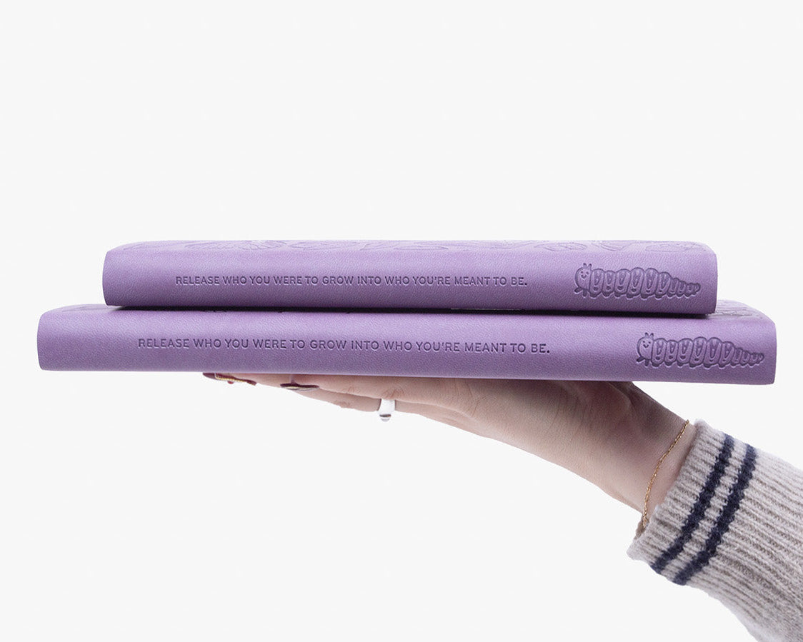 Two purple planners stacked on top of each other with a hand holding them, on a white background.