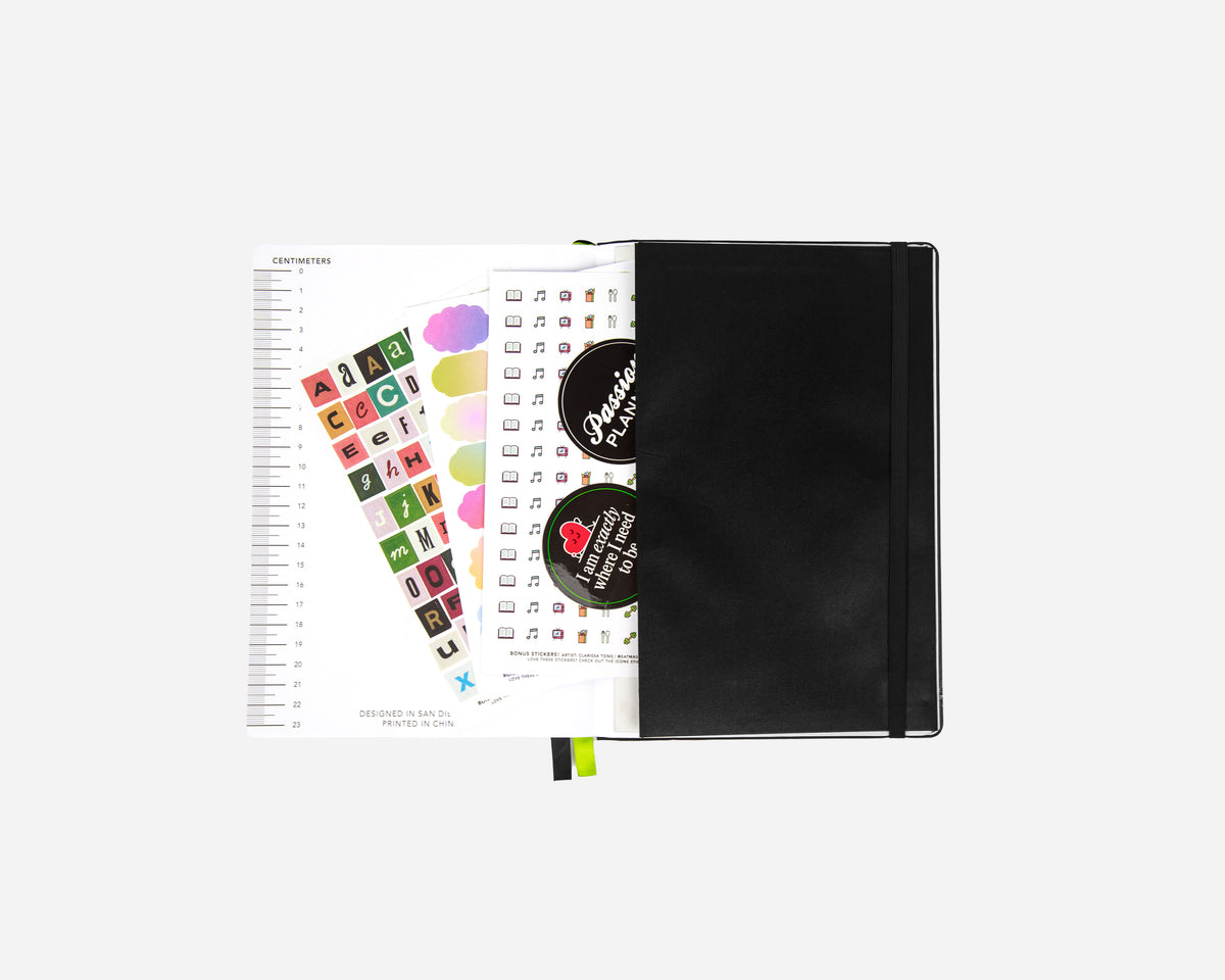 A black planner back pocket with an elastic closure partially open to reveal colorful planner stickers, photographed on a light gray background.
