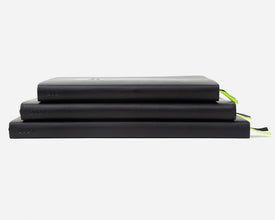 Three stacked planners in black with the year '2027' printed on the spines, and a small ribbon bookmark peeking out on the right, set against a plain white background.