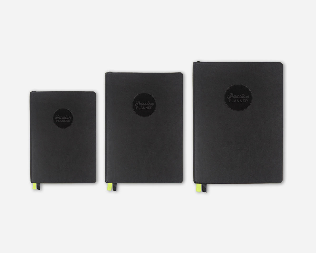 Three black faux leather 2027 planners in different sizes lined up horizontally against a light gray background. Each planner features a circular black logo on the front with the text 'Passion Planner' and a small bright green ribbon bookmark peeks out from the bottom.