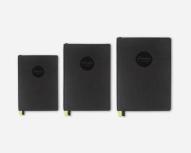 Three black faux leather 2027 planners in different sizes lined up horizontally against a light gray background. Each planner features a circular black logo on the front with the text 'Passion Planner' and a small bright green ribbon bookmark peeks out from the bottom.
