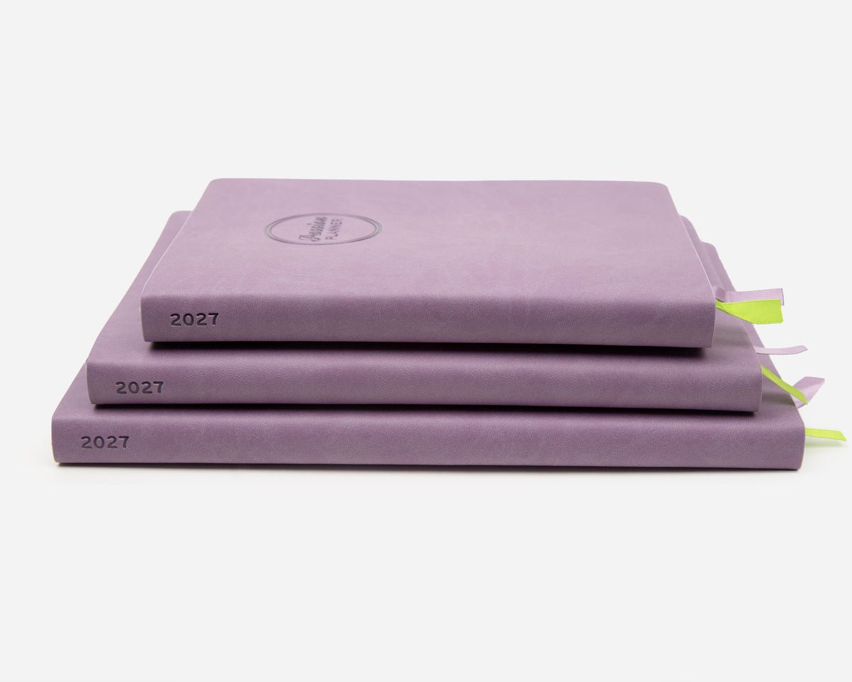 Three 2027 lavender colored planners stacked on a light gray background. 