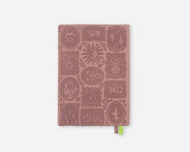 A pink mauve 2027 planner with embossed zodiac animal and celestial motifs on the cover, featuring a small green ribbon bookmark at the bottom right, shown against a light gray background.