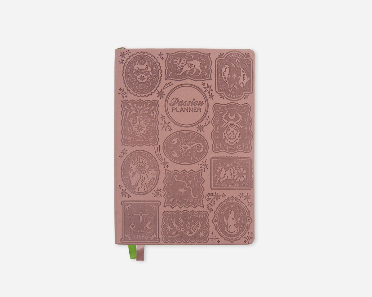 A dusty rose pink 2027 planner with embossed zodiac animal illustrations and a small green ribbon bookmark, shown on a light gray background.