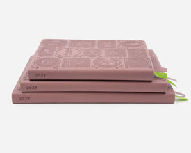Three 2027 mauve colored planners stacked on a light gray background. 