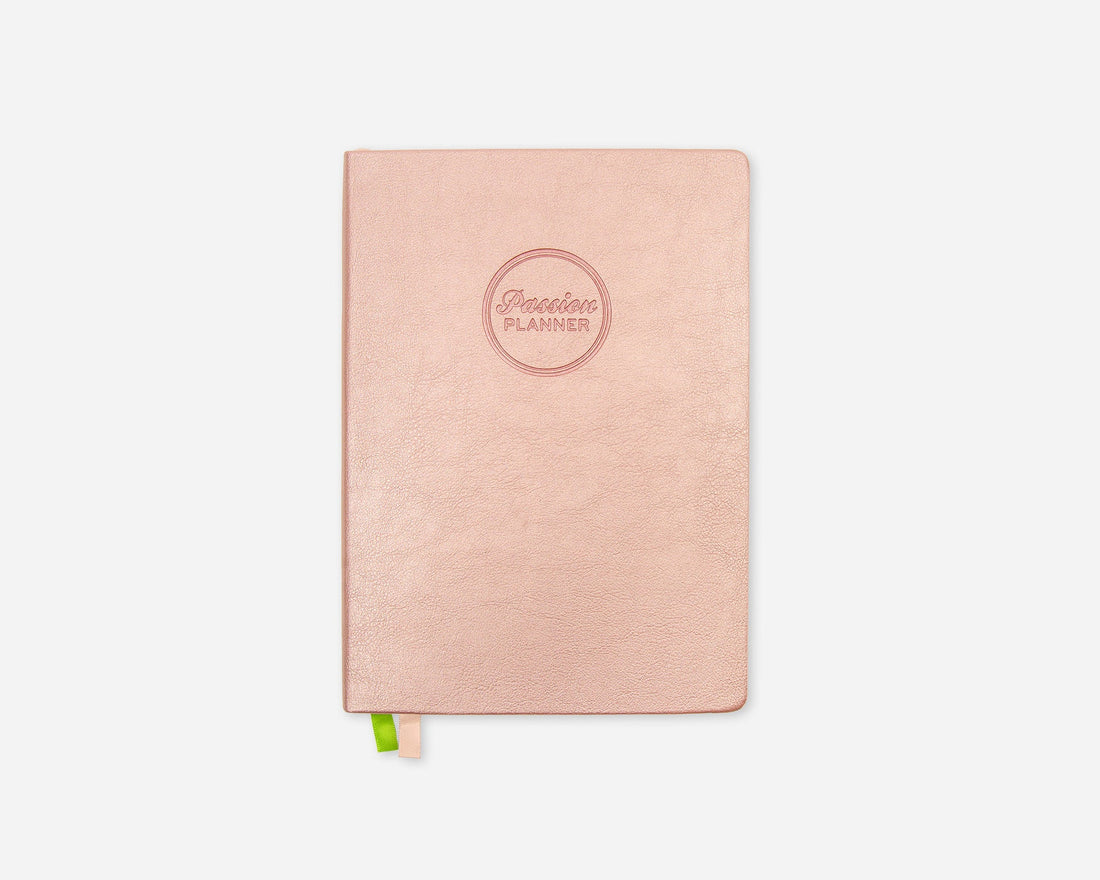 A rose gold planner with a textured faux leather cover and an embossed circular logo that reads &