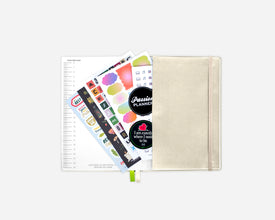 A cream-colored fabric planner sleeve with an elastic closure, shown with colorful decorative stickers. The planner features a black circular sticker with the text 'Passion Planner' and a small heart graphic.