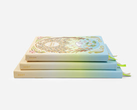 Three stacked  planners with a pastel gradient covers in cream, light green, and sky blue, each featuring decorative floral and leaf illustrations and the year 2027 on the spines, photographed on a clean white background.
