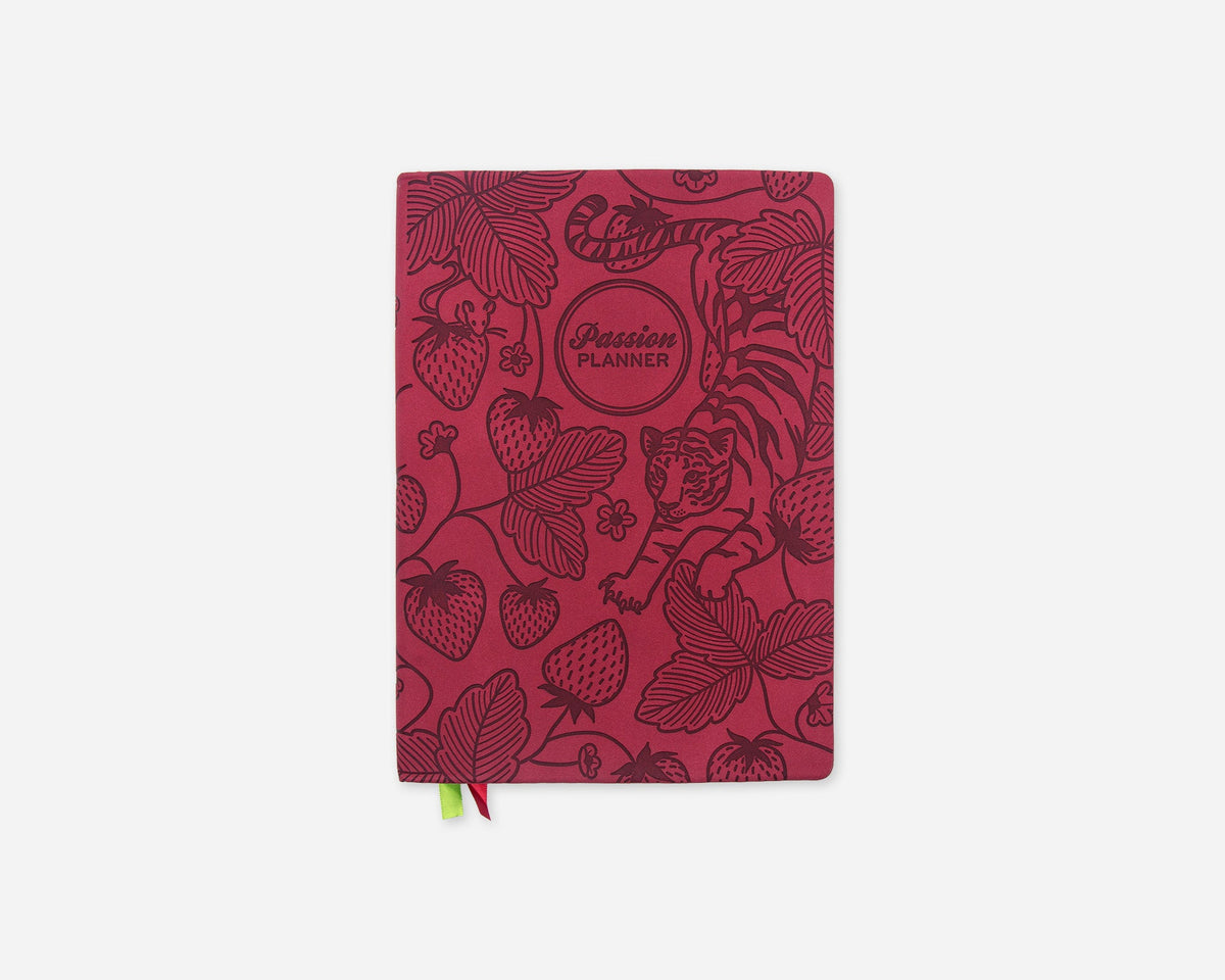 A faux leather planner with a dark red cover featuring botanical illustrations of strawberries, leaves, and a tiger, with a small green and red ribbon bookmark hanging from the bottom.