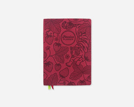 A faux leather planner with a dark red cover featuring botanical illustrations of strawberries, leaves, and a tiger, with a small green and red ribbon bookmark hanging from the bottom.