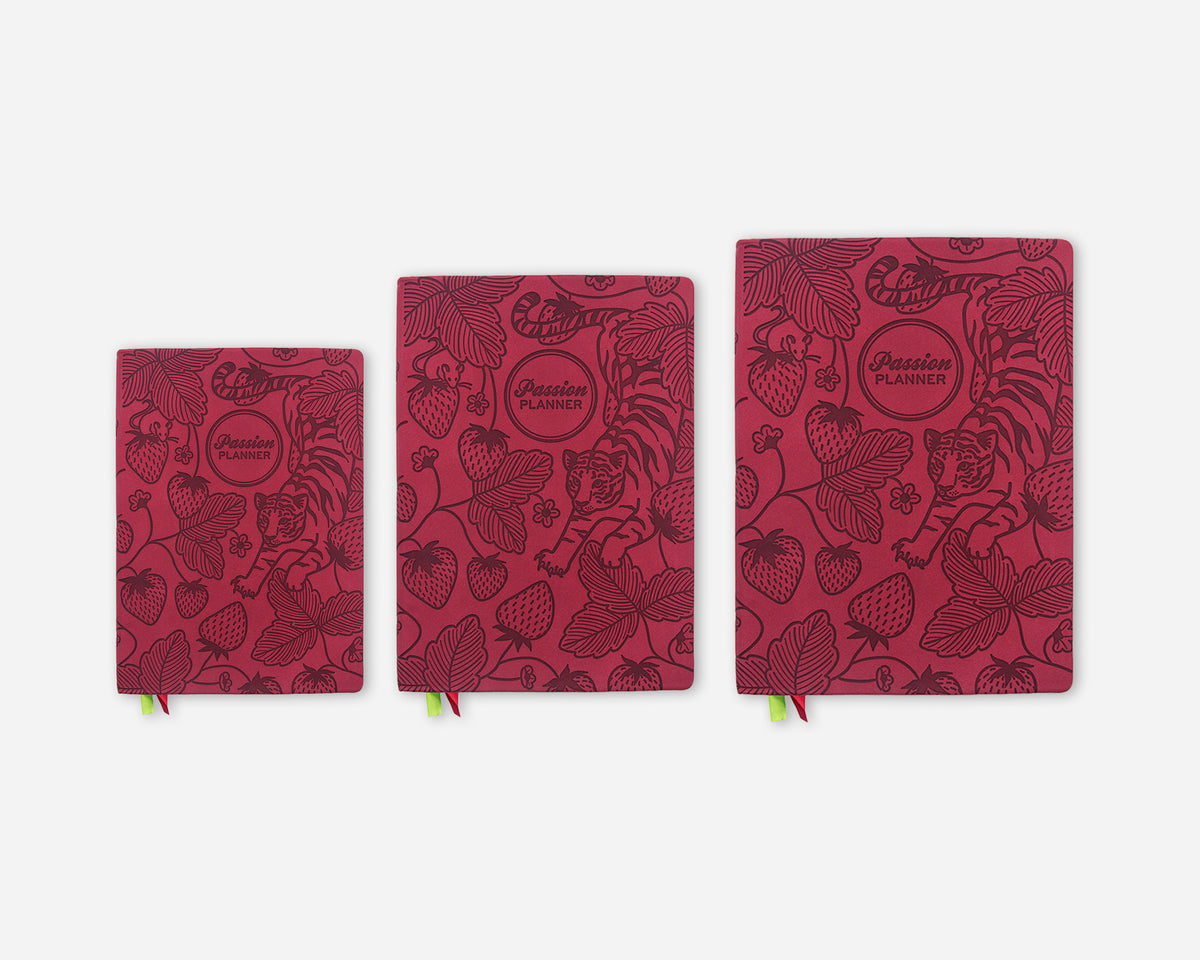 Three debossed planners in a graduated size lineup, featuring a dark red cover with a strawberry and leaf pattern and tiger illustrations.