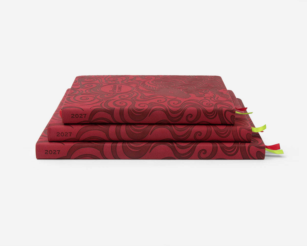 Three stacked red faux leather planners, each labeled '2027' on the spine, with small ribbon bookmarks peeking out on a clean white background.