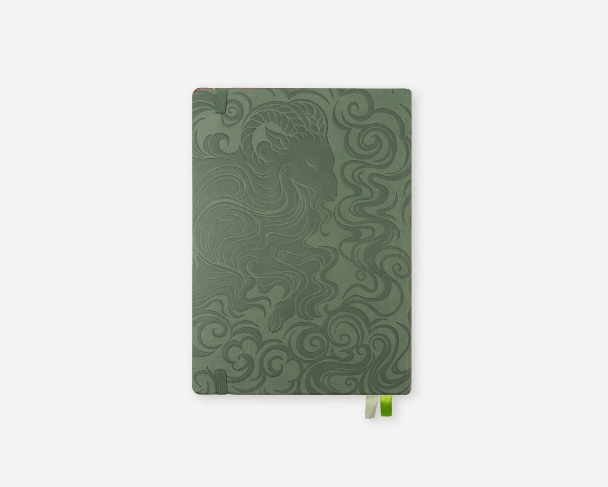 A 2027 planner with a dark sage green cover featuring an embossed swirling wave pattern and goat illustration, shown on a light gray background with a small green bookmark tab visible at the bottom right.
