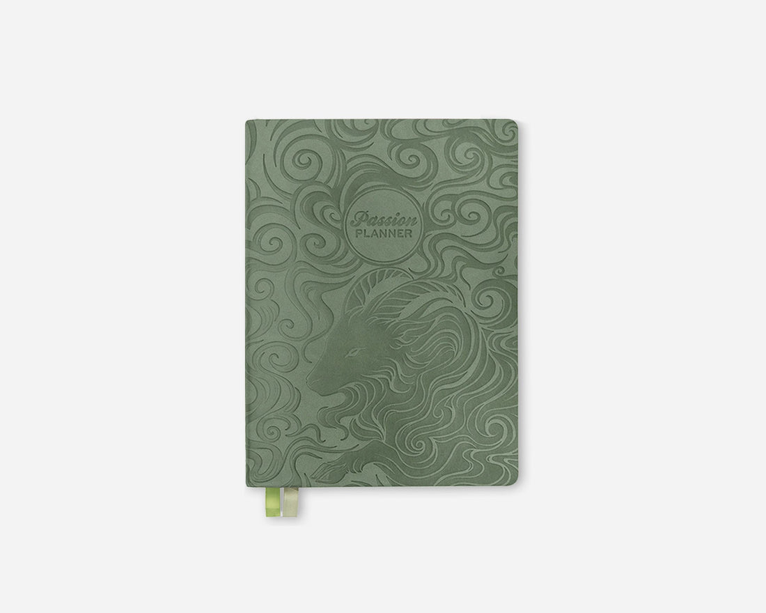 A sage green 2027 weekly planner with embossed swirl patterns and a zodiac-themed goat illustration, featuring a small green ribbon bookmark at the bottom, shown on a light gray background.