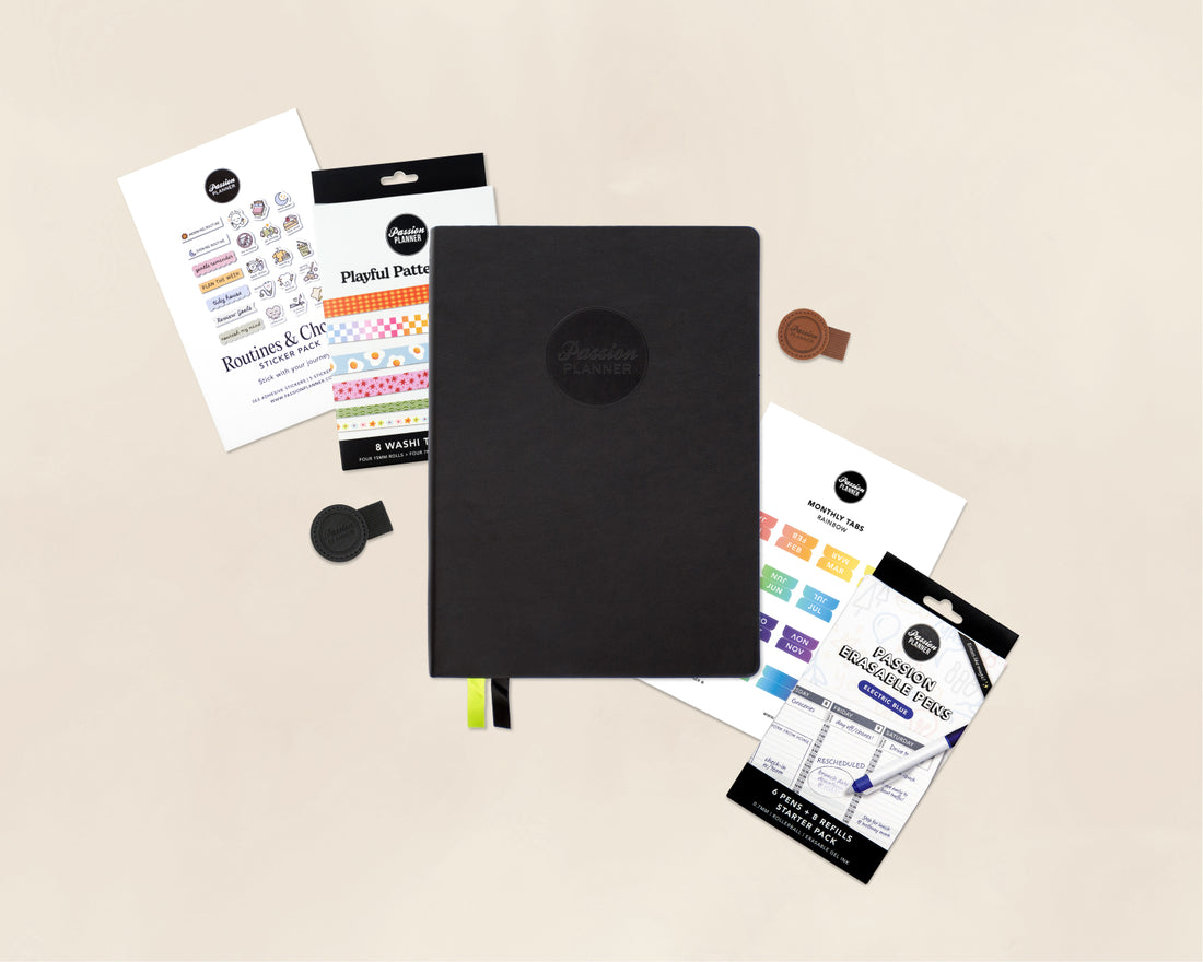 A black 2027 planner with a circular logo on the cover, arranged on a light beige background with several stationery accessories and small items around it.