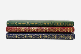 Three planners with decorative covers and years printed on them, stacked on a white background.