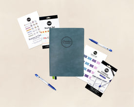 A flat-lay product shot of a planner starter set on a warm beige background. The set includes a dark teal-blue textured hardcover planner with an embossed logo, blue pens, sticker sheets, washi tape, and monthly tab stickers.