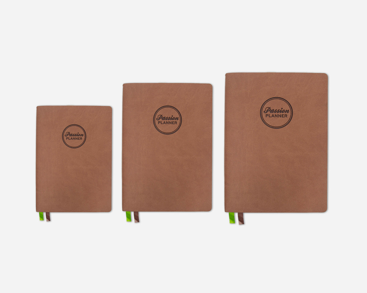 Three brown 2027 planners in different sizes lined up from smallest to largest on a light gray background. Each planner features a circular black logo that reads 'Passion Planner' and has a green and brown ribbon bookmark peeking out from the bottom.