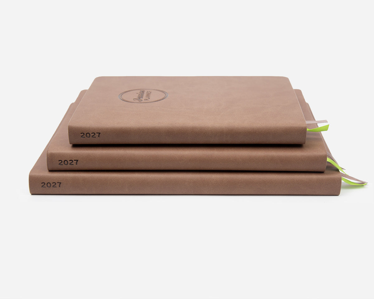 Three stacked hardcover planners in a warm brown, each labeled '2027' on the spine, with small green ribbon bookmarks visible on the right, photographed on a clean white background.