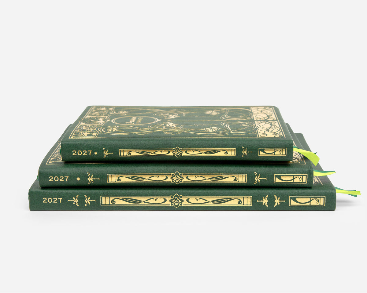 Three 2027 planners stacked on a light gray background. The books are dark green with ornate gold foil detailing on the covers and spines, and each has a bright green ribbon bookmark peeking out from the side.