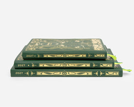 Three 2027 planners stacked on a light gray background. The books are dark green with ornate gold foil detailing on the covers and spines, and each has a bright green ribbon bookmark peeking out from the side.