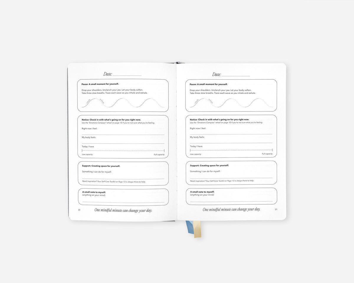 An open Mindful Minute Journal showing two inner pages with lined writing sections and a small blue ribbon bookmark, photographed on a clean light gray background.