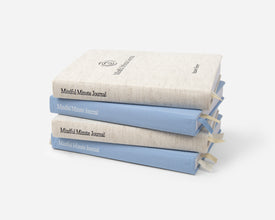 A stack of 4 Mindful Minute Journals in linen and blue on a gray background.