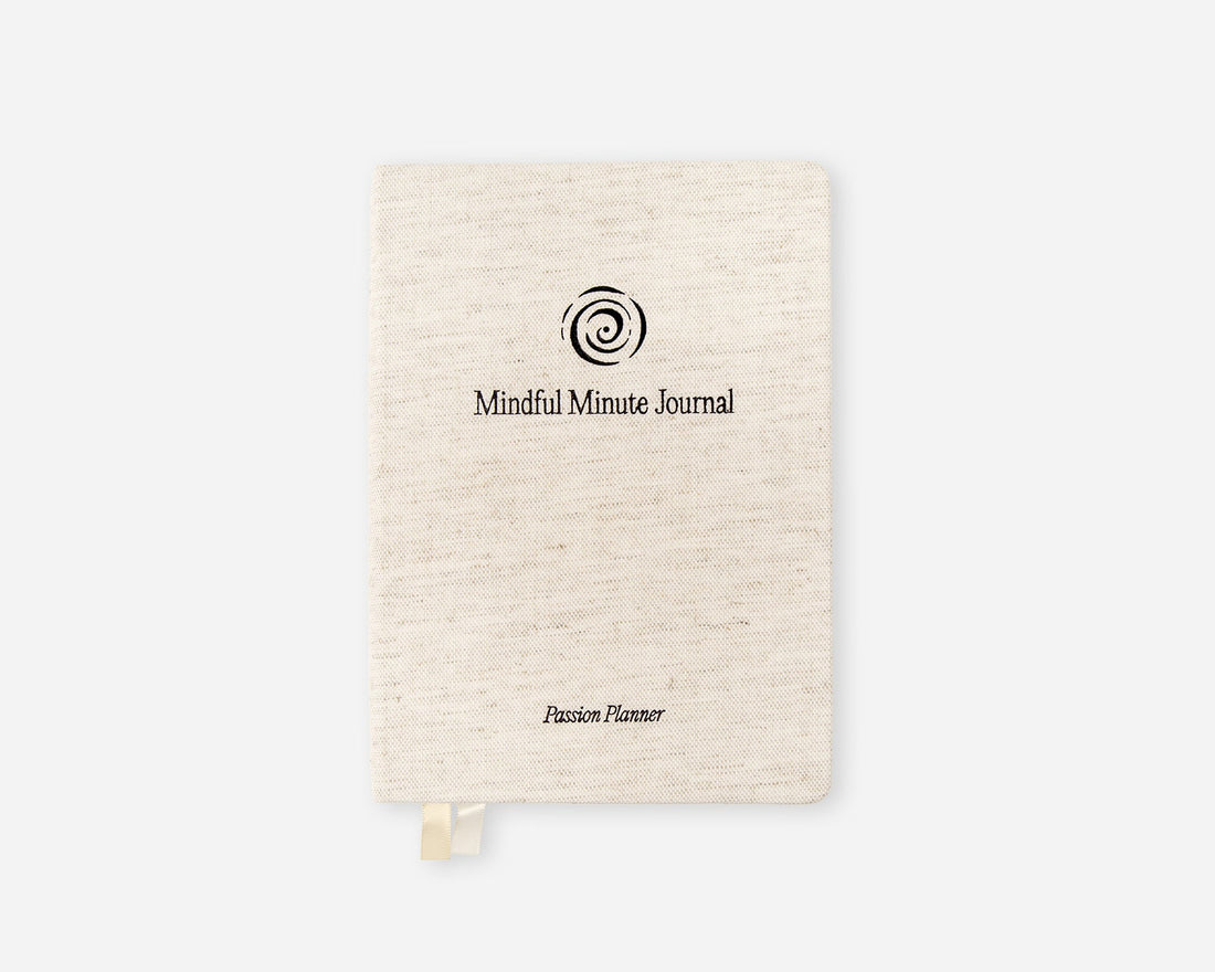 A cream-colored linen-textured hardcover journal with a black spiral logo and the text &