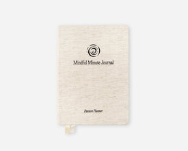 A cream-colored linen-textured hardcover journal with a black spiral logo and the text 'Mindful Minute Journal' and 'Passion Planner' on the front, shown on a light gray background.