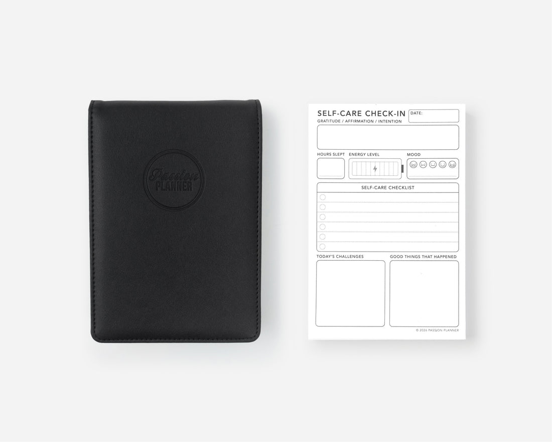 A black leather self-care notebook cover with an embossed circular logo next to a white &