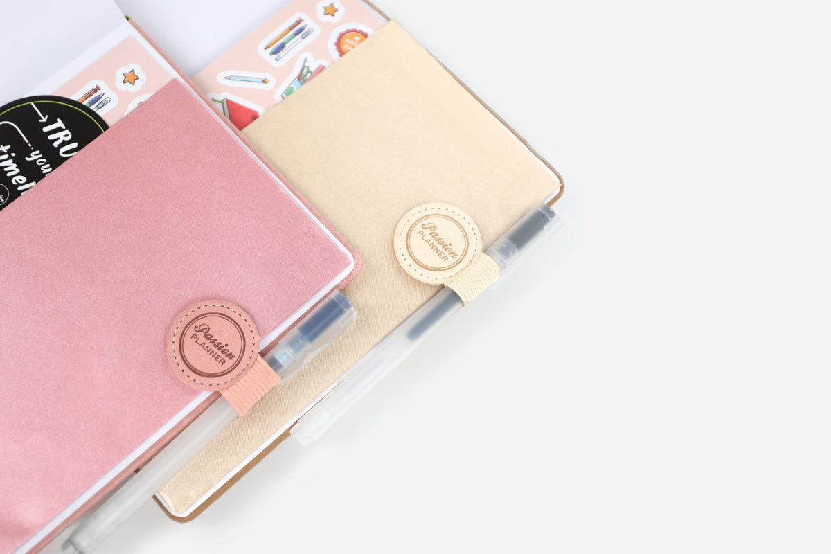 Pink and beige planners with faux leather pen loops on a white surface