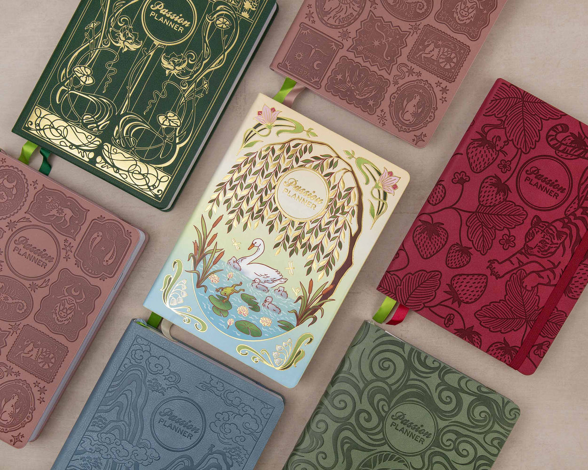 Seven decorative notebooks arranged in a flat lay on a light beige surface. Each notebook has embossed or printed floral and ornamental patterns, a green ribbon bookmark, and the circular logo 'Passion Planner'.