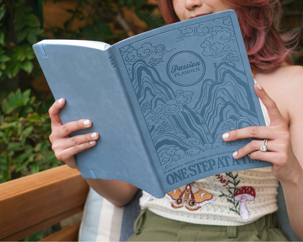 A person holding an open blue faux leather 2027 planner titled &