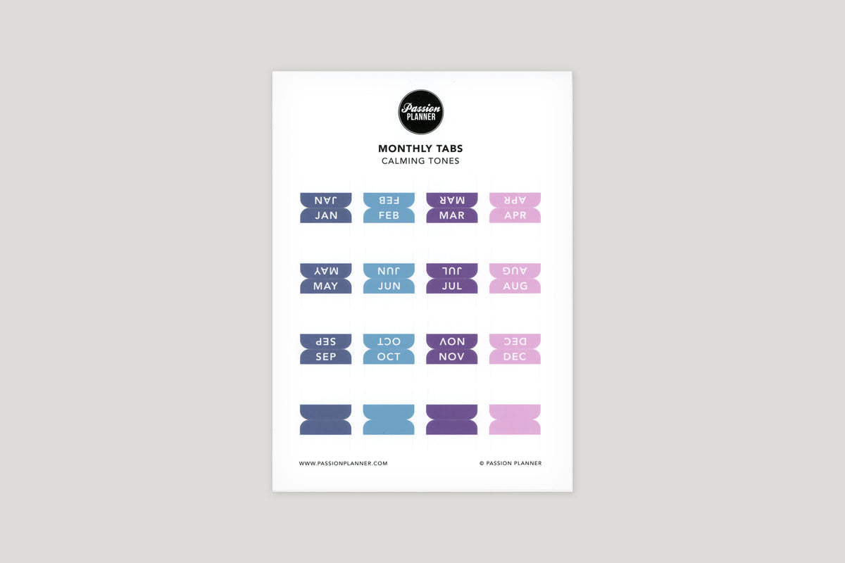 A sheet of cool toned multi-colored monthly tabs labeled with different months of the year, designed to be used in a planner.